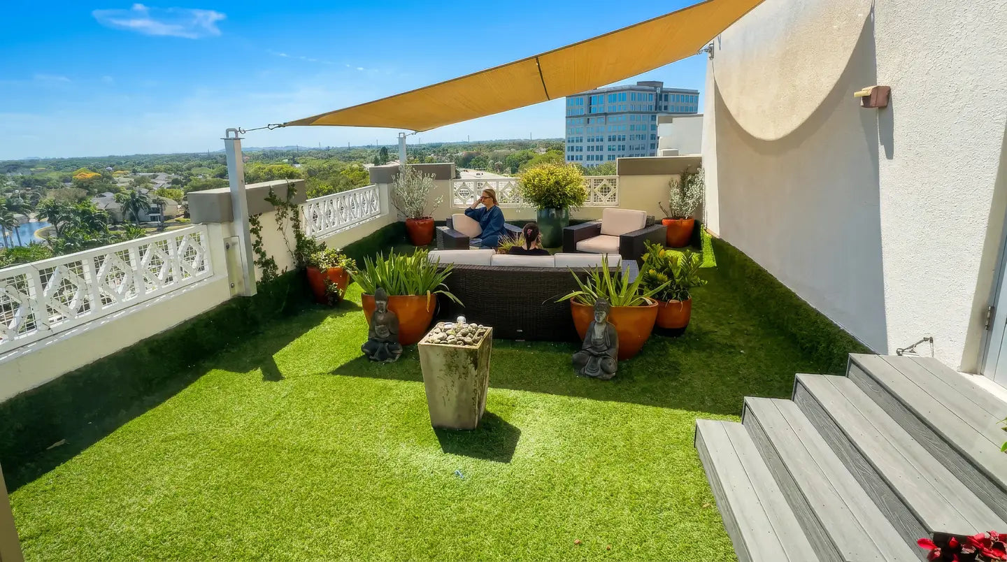 Salon Sora's 7th-floor rooftop garden in Boca Raton: turf lawn, Buddha statues, potted plants and skyline views (AI-enhanced photo)